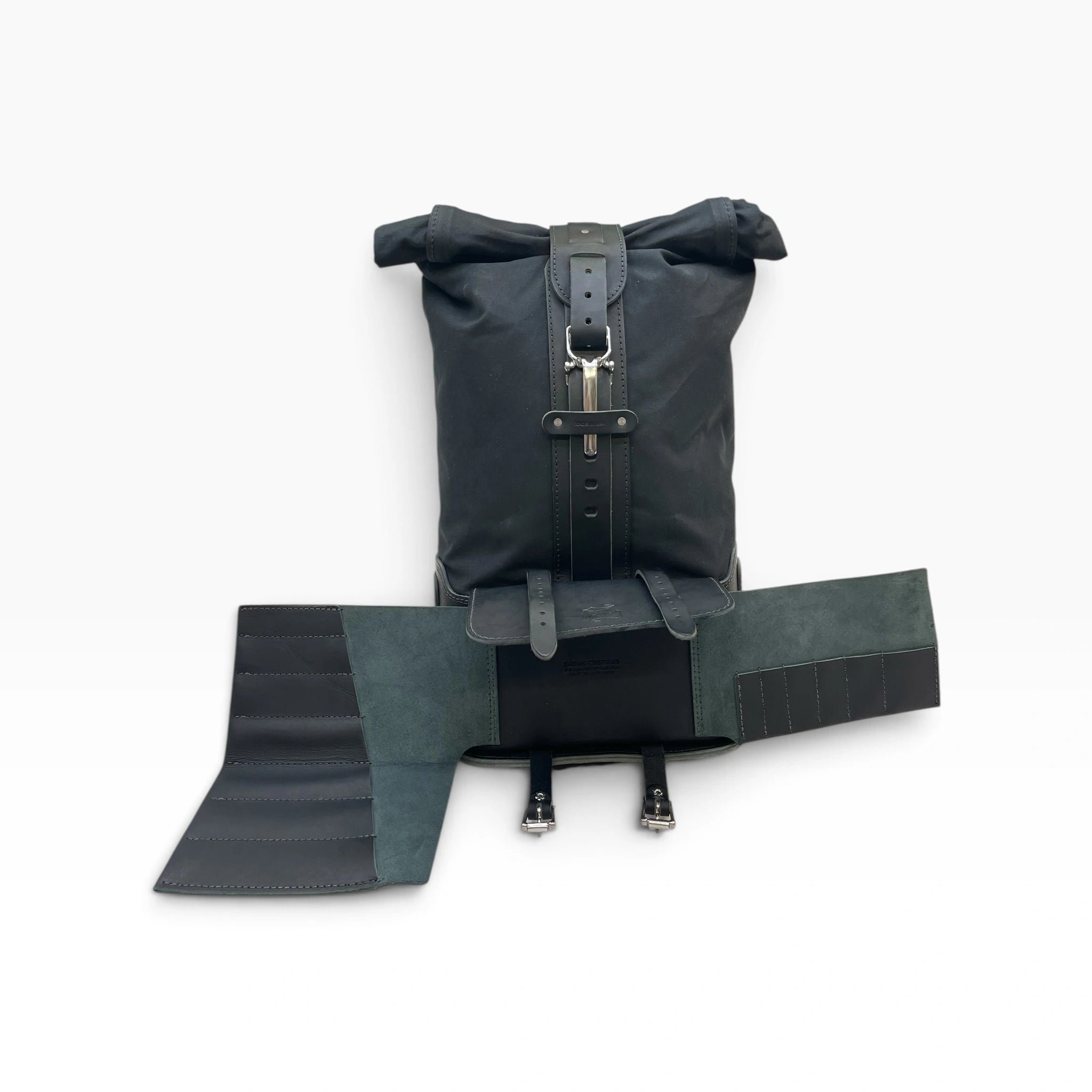 A black waterproof roll-top backpack with a matching black leather buckle strap, shown with its attached black and dark green fabric pouch or organizer laid out in front on a white background.